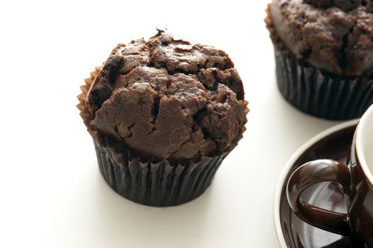 Tasty freshly baked double chocolate muffins next to cropped coffee cup on white table