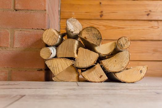 Birch firewood lies on the floor of a wooden house near the fireplace to heat the house on cold days..