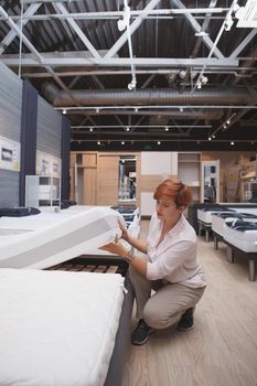 Vertical full length shot of a female customer examining orthopedic mattress on sale at home goods mall