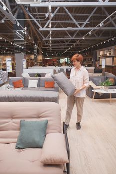 Vertical shot of a female customer examining couch cushion, shopping at furnishings store