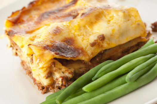 Close up Tasty Lasagna Recipe with Green String Beans on the Side, Served on White Plate.