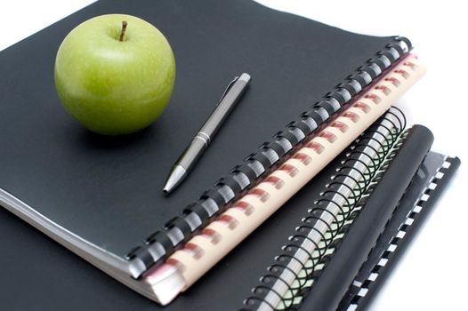 Spiral bound notebooks for taking university notes topped with a pen and fresh healthy green apple to eat as a snack while studying