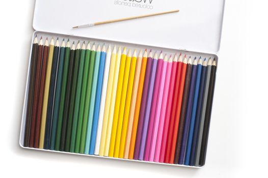 Angled top down view on open white tray full of various colored pencils and paintbrush over white background with slight drop shadow
