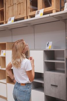 Vertical shot of a female customer looking at hselves and cupboards on sale at furniture store