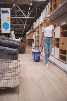 Vertical full length shot of a mature woman walking in furniture store with her cart, enjoying shopping