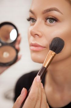 Cropped vertical closeup of makeup artist applying highlighter on cheekbones of a gorgeous female