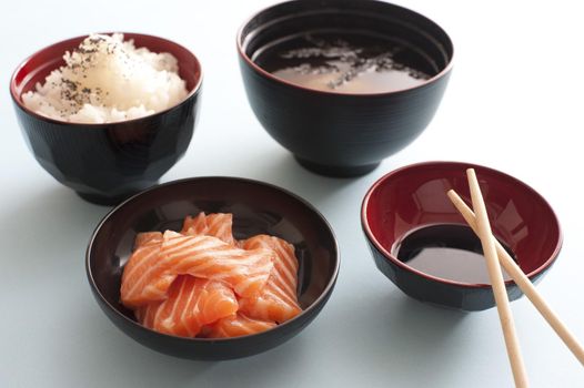 Raw salmon sashimi with soy sauce and a side dish of rice served with Asian chopsticks in individual bowls