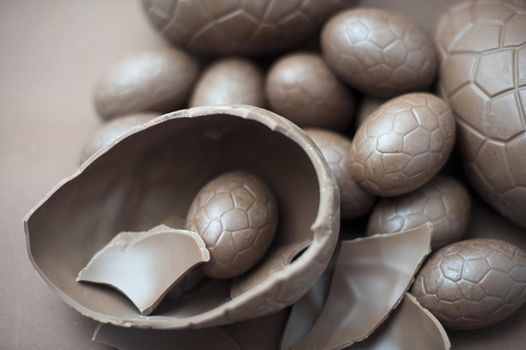 Cracked milk chocolate Easter egg accompanied by a collection of various sized eggs on a brown background