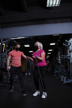 Vertical full length shot of a senior woman and her fintess coach wearing medical face masks at the gym