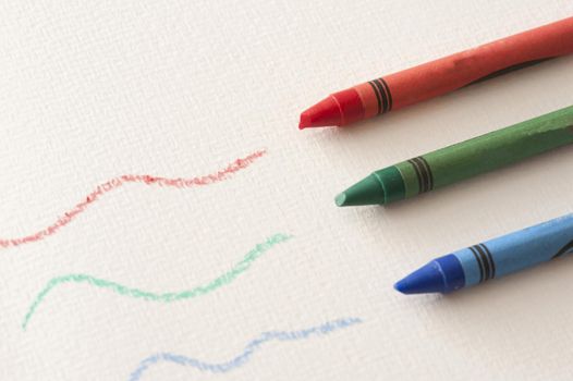 Green, red and blue colored wax crayons with squiggly hand drawn lines over textured paper viewed high angle