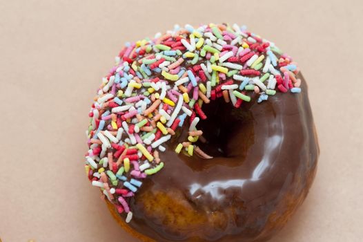Delicious fresh chocolate ring donut with colorful sprinkles on a beige background with copyspace, overhead view