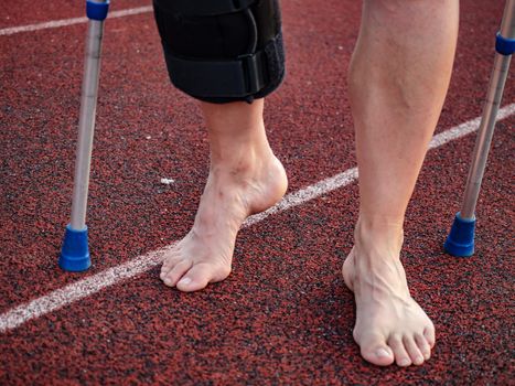 Walk by crutches. Woman runner got sports injury running on stadium trail 