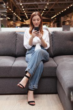 Vertical full length shot of a woman using smart phone, sitting on a couch