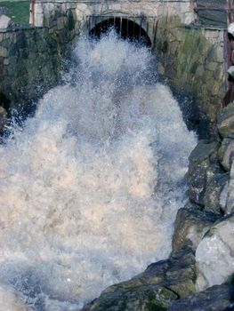 White frothy water gushing from a stormwater culvert with great force into a channel during flooding