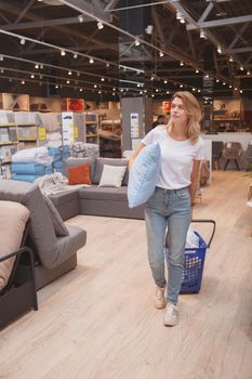 Vertical full length shot of a mature woman carrying pillow, shopping at furniture store