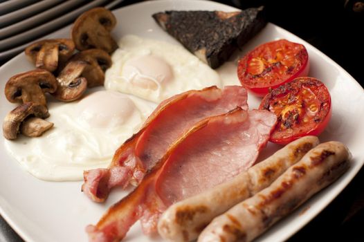 Wholesome cooked English breakfast with fried eggs, grilled bacon, sausages, mushrooms, plack pudding and tomato for a hearty diet