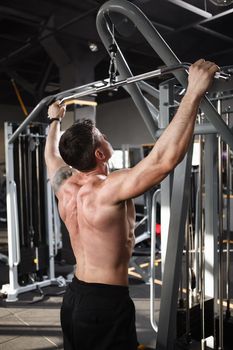 Vertical rear view shot of a ripped muscular male athlete exercising on lat pull down machine