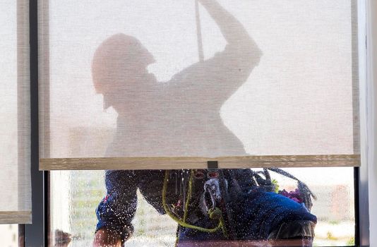 Silhouette of a rope access glass cleaner working at heights.