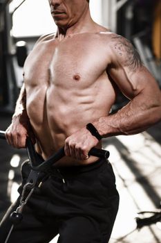 Cropped vertical shot of a muscular bodybuilder working out in crossover gym machine