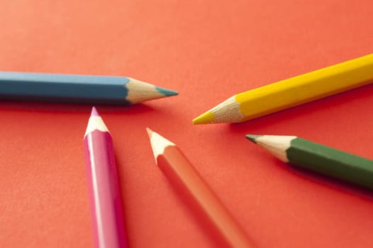 Close up of five colored pencils, yellow, red, pink, blue and green, over orange background
