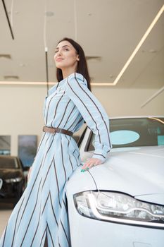 Vertical shot of an elegant woman leaning on a new car she bought