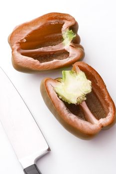 Sliced halved fresh raw red capsicum or bell pepper lying on a white background with a knife alongside during preparation of the vegetable