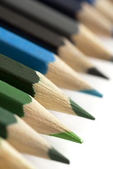 Line of colored pencil crayons with close up focus to the sharpened point of the green pencil isolated on white