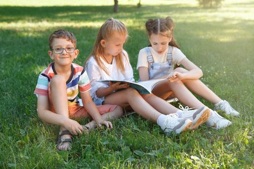 Funny young boy smiling to the camera sitting on the grass with his friends