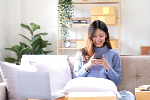 Asian business woman on sofa using a laptop computer checking customer order online shipping boxes at home. Starting SME Small business entrepreneur freelance. Online business, SME Work home concept..