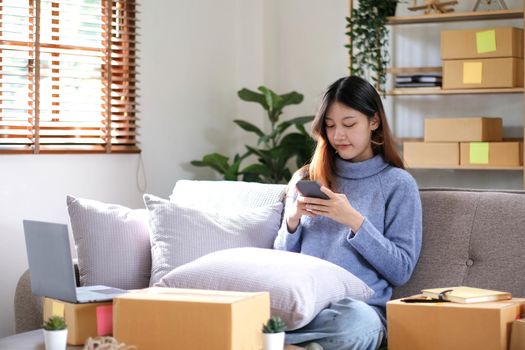 Asian business woman on sofa using a laptop computer checking customer order online shipping boxes at home. Starting SME Small business entrepreneur freelance. Online business, SME Work home concept..