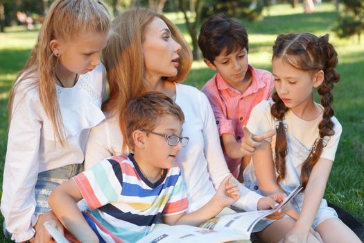 Young attractive female teacher reading a book to her little students