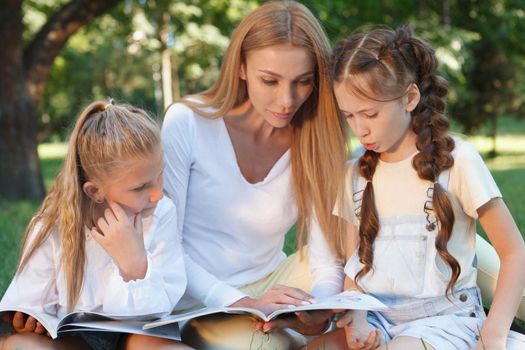 Lovely teacher and her female pupils reading together in the park