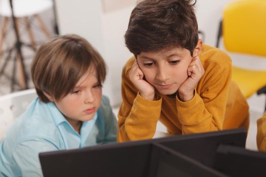 Two little schoolboys working together on a computer at school