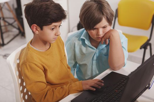 Top view shot of two young boys using laptop together, studying at school