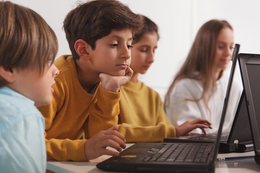 Close up of a cute little Arab boy looking focused, working on a project on his laptop at school