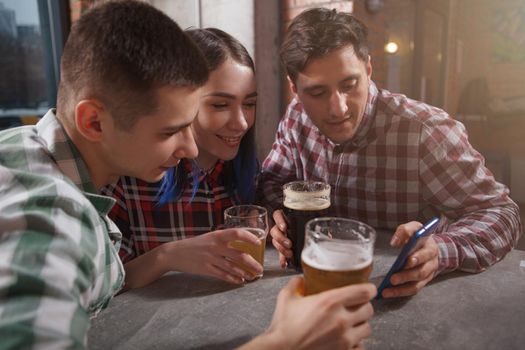 Group of friends watching something on smart phone, drinking beer together at the pub