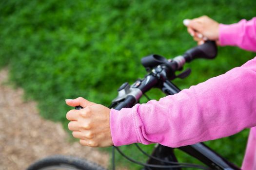 A girl in a pink sweatshirt holds on to the handlebars of a bicycle, a bike ride in the park. Outdoor recreation is good for health