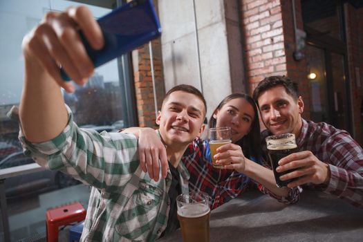Group of young people taking selfies while drinking beer together at the pub