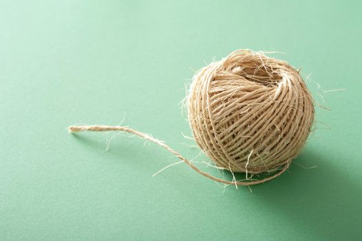 Small clew of jute threads of natural linen or ball of rustic strings viewed in close-up on pale green background