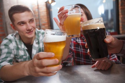 Selective focus on beer glasses in the hands of young people celebrating at beer pub