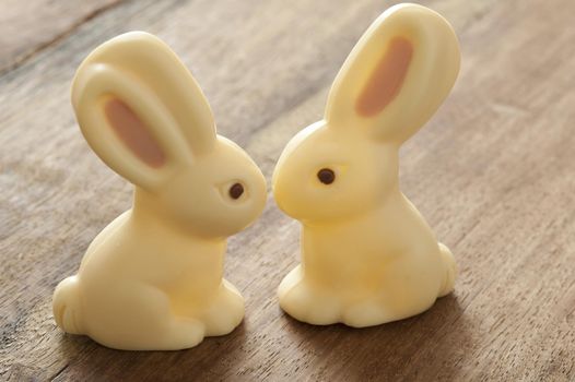Close-up of two Easter bunny candies of white chocolate sitting on wooden table close, as if kissing