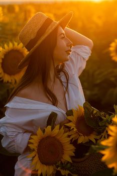 A girl in a hat on a beautiful field of sunflowers against the sky in the evening light of a summer sunset. Sunbeams through the flower field. Natural background