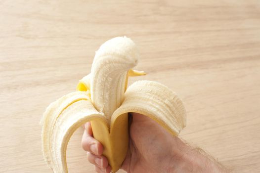 Uncorked banana in man's hand against of wooden background