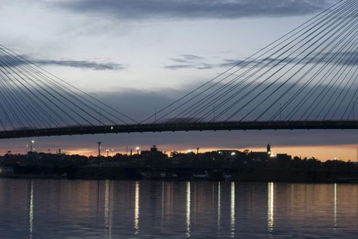 The middle of suspension bridge deck over water in twilight with the lights reflecting in calm water surface