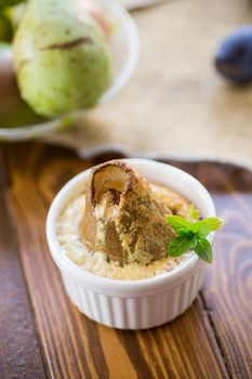 pear baked in curd dough in a small ceramic form, on a wooden table.