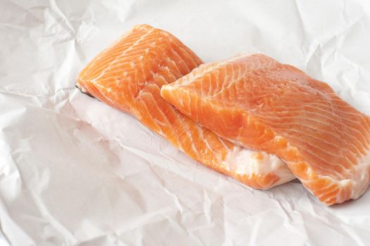 Two chunks of raw pink salmon meat on top of each other in white unwrapped butcher paper