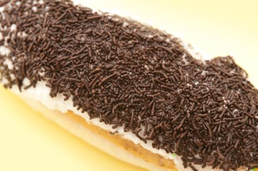Sticky bun with a creamy glaze decorated with a coating of chocolate candy sprinkles, closeup view of the texture of the sprinkles from a high angle
