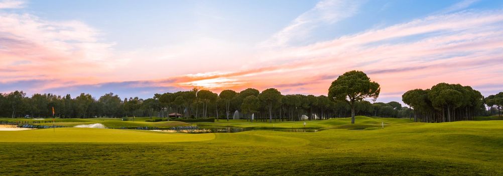 Panoramic view of beautifPanoramic view of beautiful golf course with pines at sunset. Golf field with fairway, lake and pines