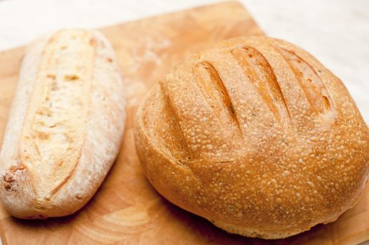 Two freshly baked uncut crusty loaves of bread, one round and one long, on a wooden bread board