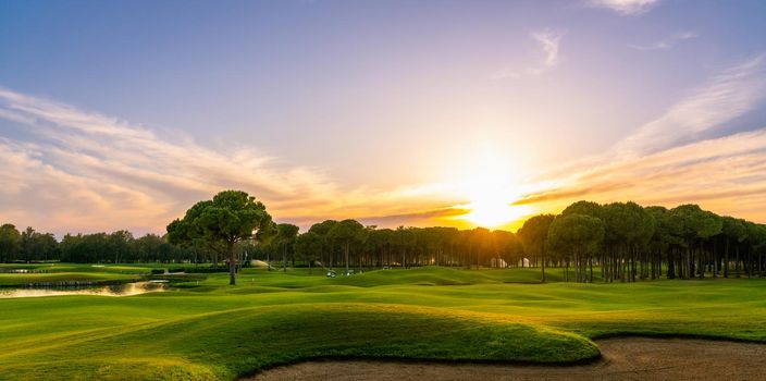 Golf course at sunset with beautiful sky. Scenic panoramic view of golf fairway